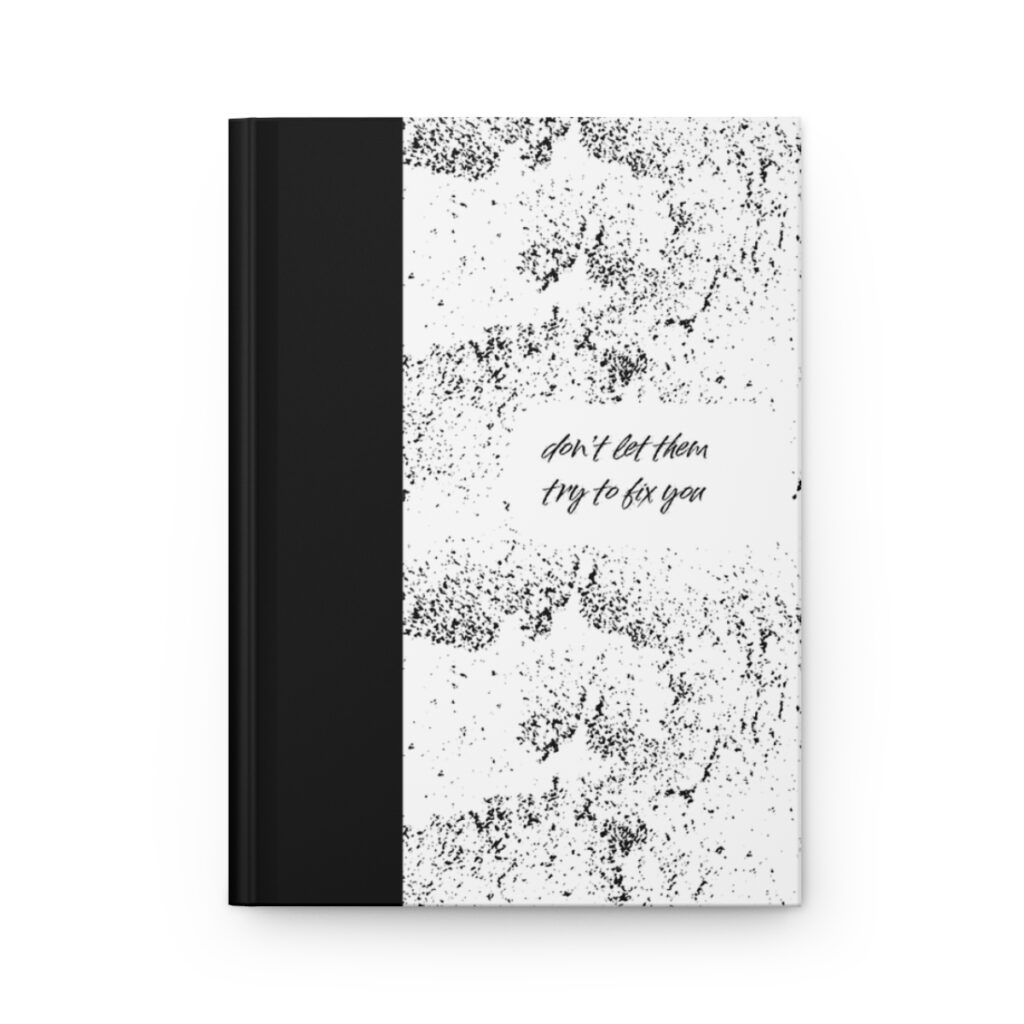 A notebook with a black spine and a white cover featuring abstract black speckles. Centered text reads, "don't let them try to fix you." The tone is empowering. by  iziiexpressions.com