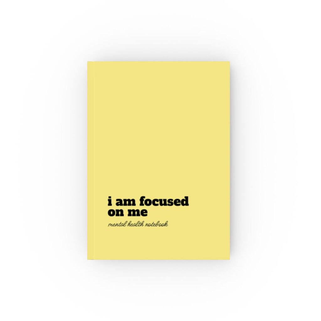 An yellow hardcover notebook cover with bold black text reading "i am focused on me." Below, smaller text says "mental health notebook." The tone is empowering by iziiexpressions.com