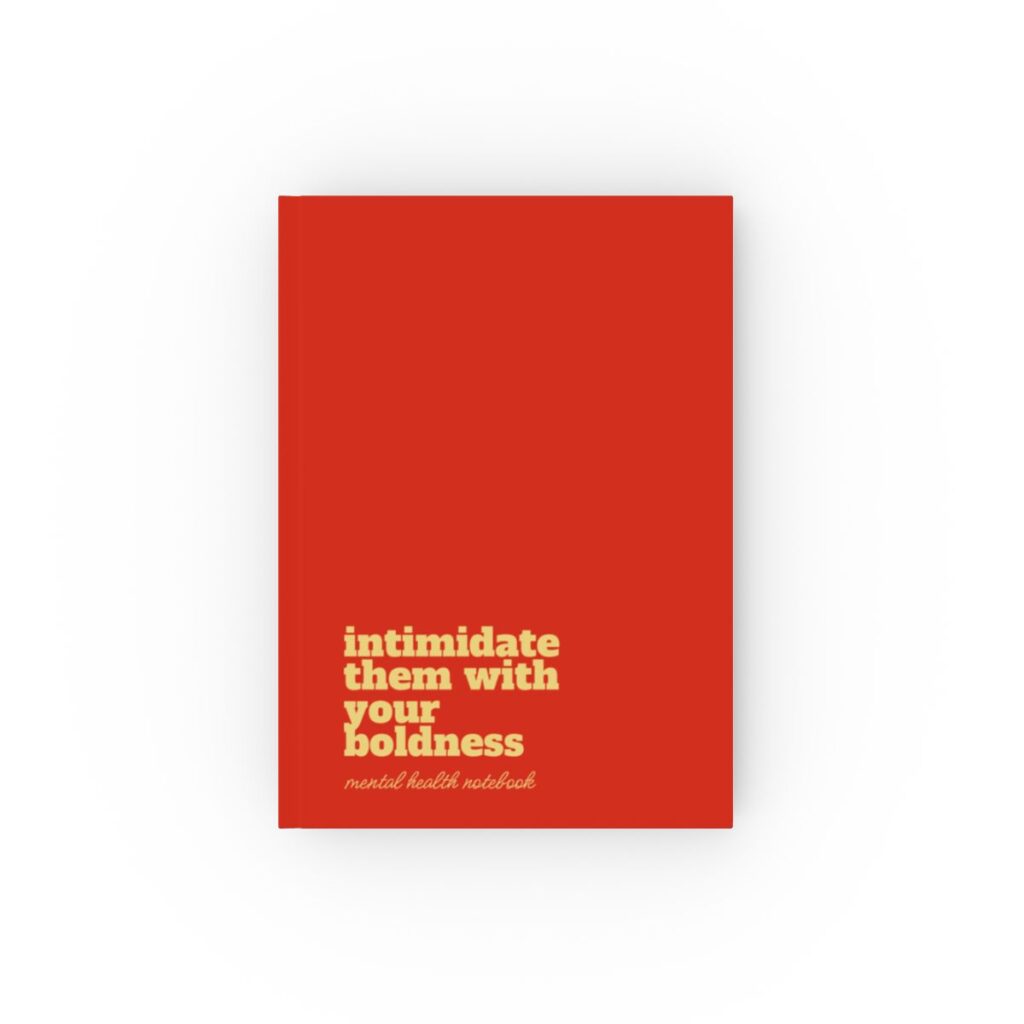 An sunset red hardcover notebook cover with bold yellow text reading "intimidate them with your boldness." Below, smaller text says "mental health notebook." The tone is empowering by iziiexpressions.com