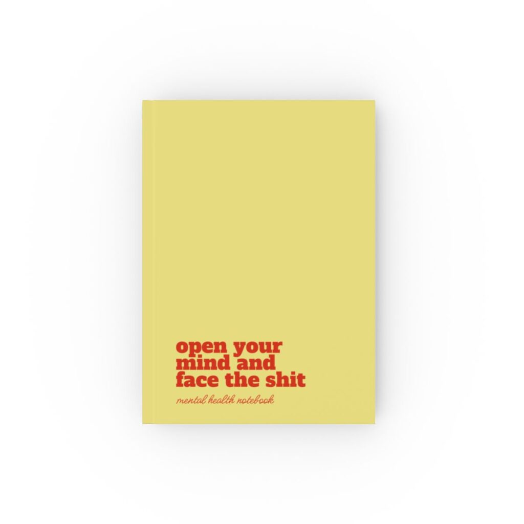 An yellow hardcover notebook cover with bold red text reading "open your mind and face the shit." Below, smaller text says "mental health notebook." The tone is empowering by iziiexpressions.com