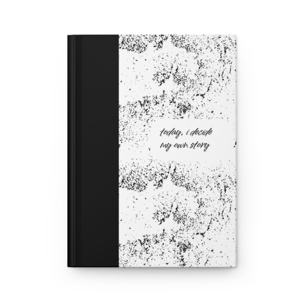 A notebook with a black spine and a white cover featuring abstract black speckles. Centered text reads, "today, i decide my own story." The tone is empowering, by iziiexpressions.com