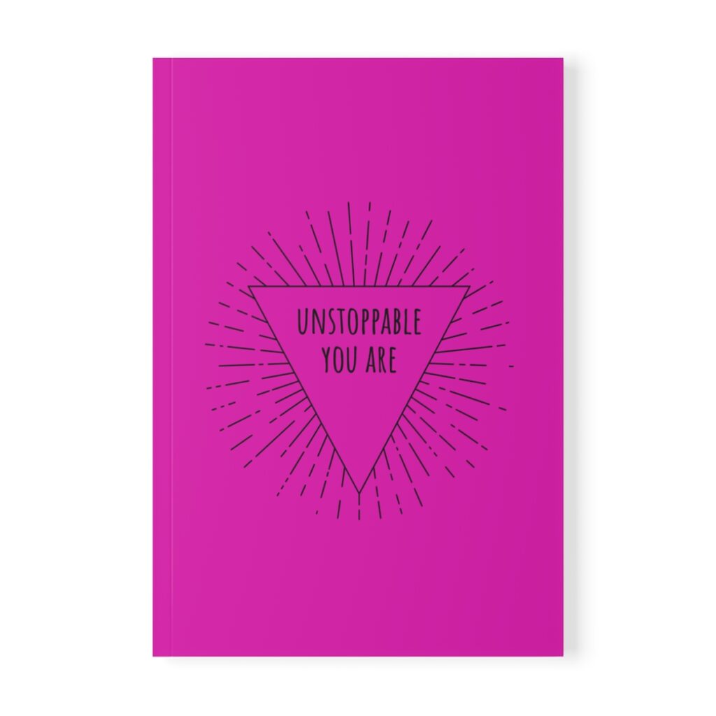 Pink softcover notebook with a black triangle in the center. Inside the triangle, the text reads "Unstoppable You Are" with radiating lines around it, conveying motivation by iziiexpressions.com