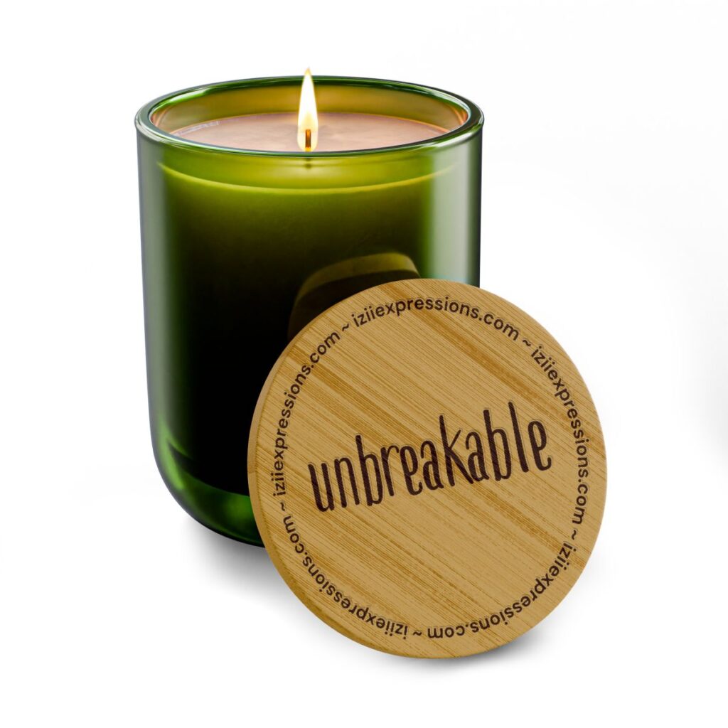A lit green glass candle with a wooden lid engraved with "unbreakable."